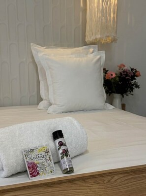 A neatly made bed with white linens, a white towel, and a bottle of perfume on the bed. - Palm Tree (Cannes)
