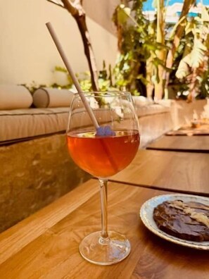 Ein Glas roter Drink mit Trinkhalm auf einem Holztisch, ein Teller mit Schokoaufstrich und eine Couch im Hintergrund.