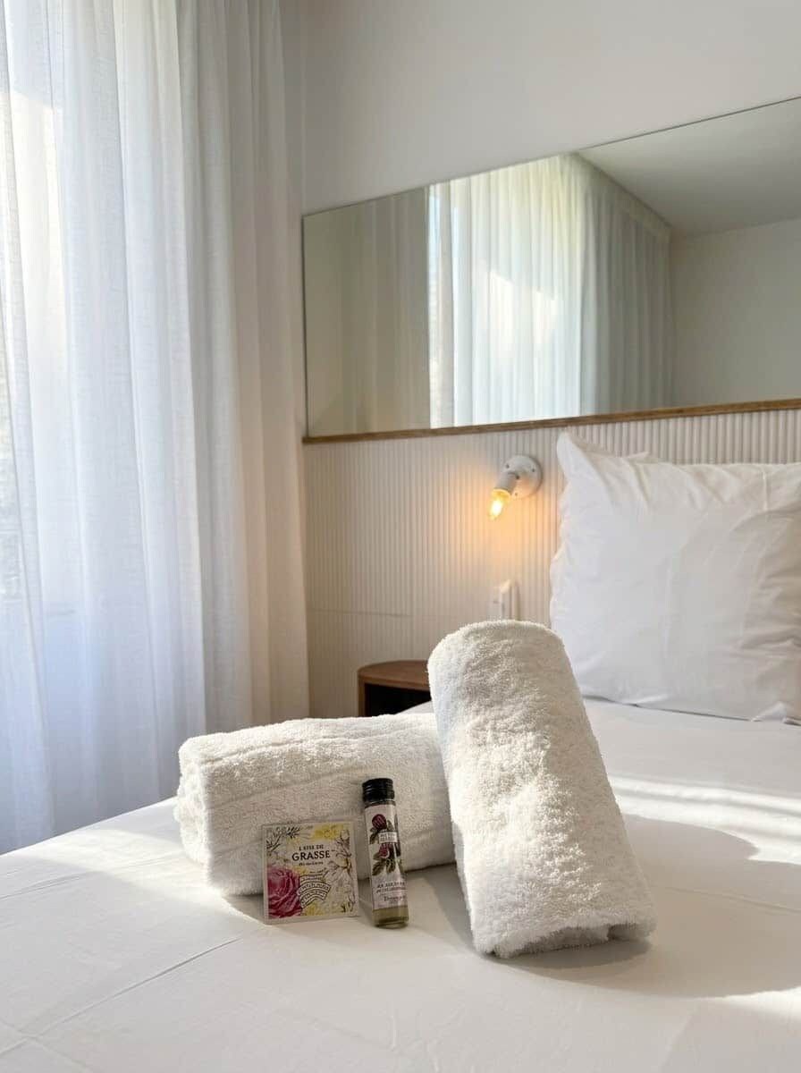 A hotel room with a neatly made bed, a bedside lamp, and a bottle of lotion on the bed.