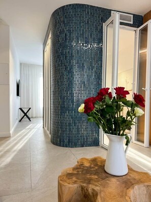 A modern interior with a curved wall, a white vase with red and white flowers, and a wooden table. - Jasmin (Cannes)