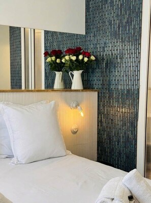 Ein Hotelzimmer mit einem Bett, einem Nachttisch, einer Vase mit Blumen und einer Wand mit vertikalem Muster.