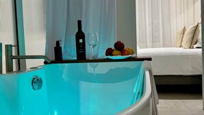 Een moderne badkamer met een ruime badkuip, een douchecabine met glazen wanden en een nachtkastje met fles, glas en fruit.