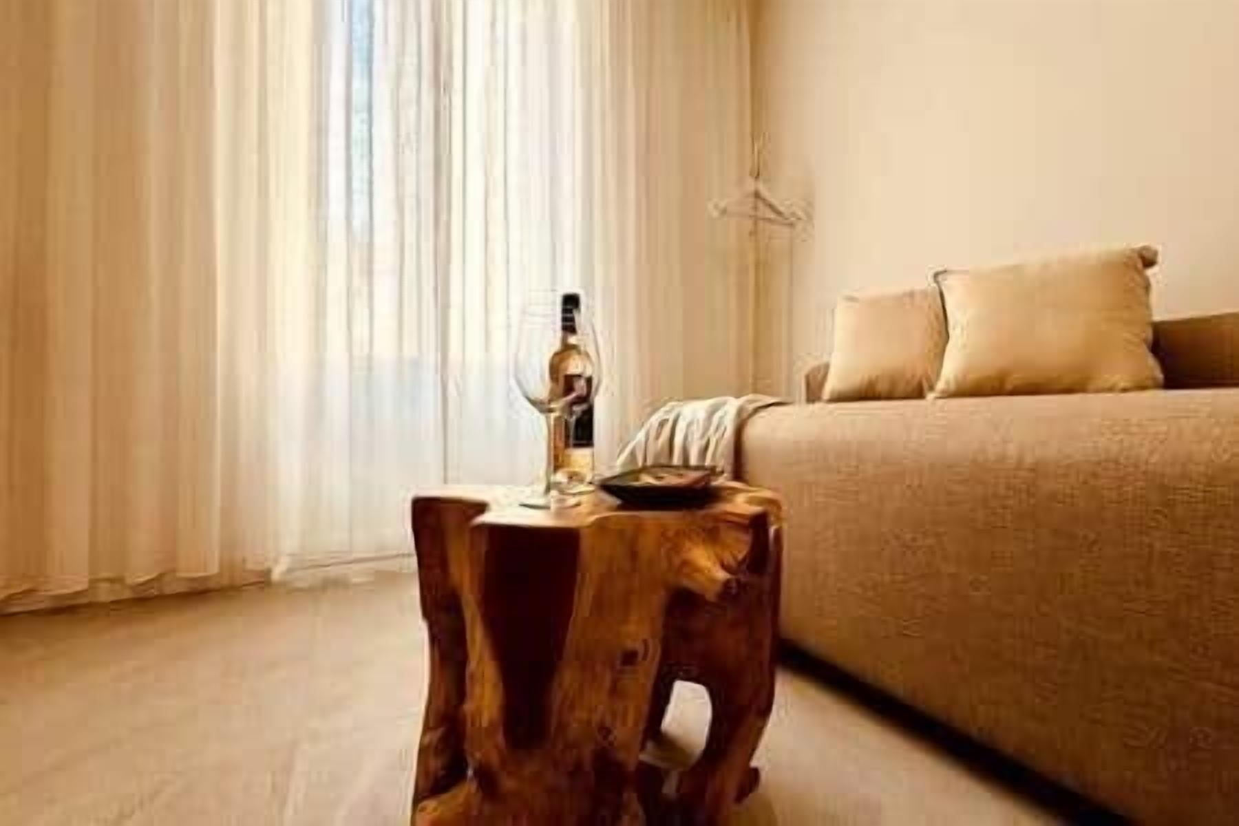 Une chambre à coucher avec un lit, un tabouret en bois et une fenêtre avec des rideaux.