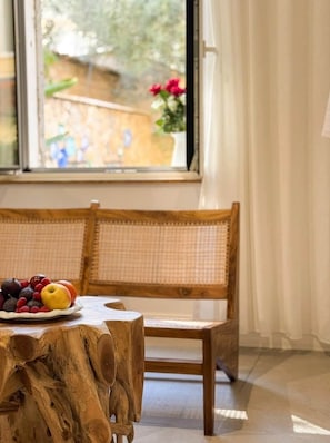 A wooden dining table with a fruit plate, a wicker chair, and a window with curtains. - Jasmin (Cannes)