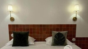 Et hotelværelse med en seng, to væglamper og en flisebeklædt sengegavl.