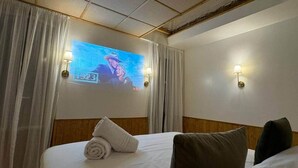 Et hotelværelse med en seng, gardiner, et vægmonteret fjernsyn og to væglamper.