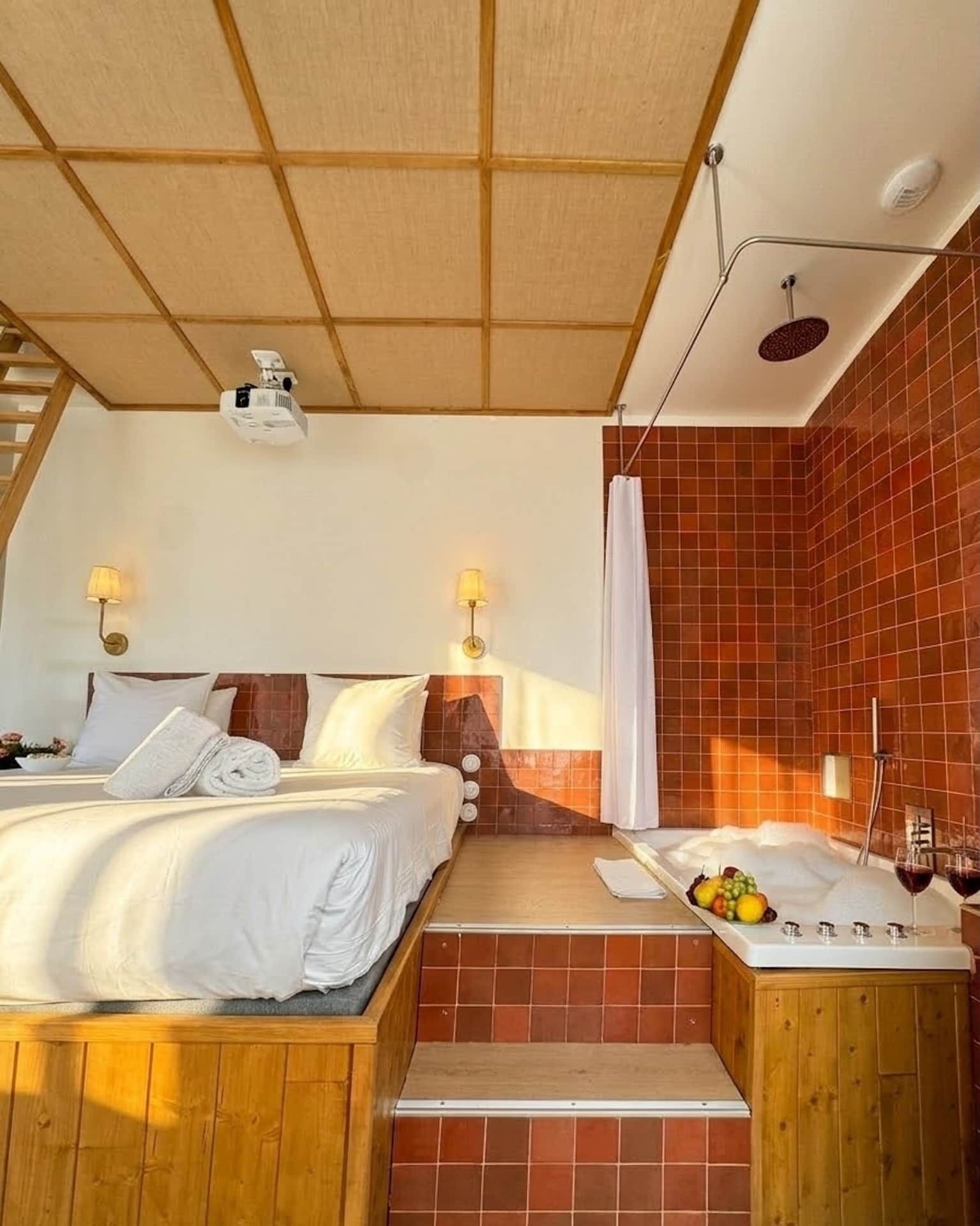 A bedroom with a bed, a nightstand, a shower, and a staircase.