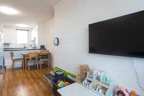 A room with a wooden floor, a desk with chairs, a television mounted on the wall, and a teddy bear on a shelf. - Cosy 2 BDR APT in heart of Fremantle with Parking (Fremantle)