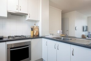 A modern kitchen with white cabinets, stainless steel appliances, and a black countertop. - Cosy 2 BDR APT in heart of Fremantle with Parking (Fremantle)