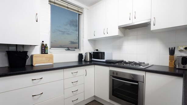Una cucina moderna con mobili bianchi, un piano di lavoro nero, un fornello, un forno e una finestra con vista.
