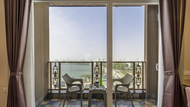 Ein Balkon mit zwei Stühlen und einem Tisch, mit Blick auf ein Gewässer und Gebäude.