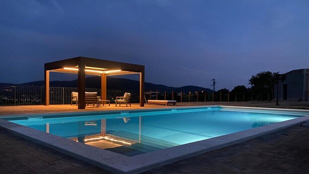 Una piscina rectangular con una zona de estar cubierta y sillas de descanso.