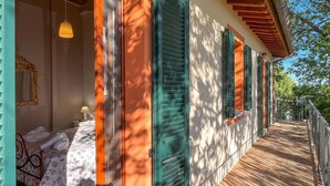 Habitación de hotel con cama, mesita de noche y lámpara. Incluye un balcón con piso de madera y barandilla.