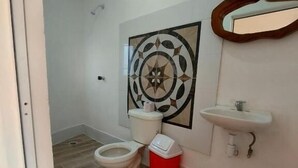 Une salle de bain comprenant des toilettes, une poubelle rouge, un lavabo et un élément décoratif mural.