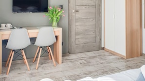 Ein Schlafzimmer mit einem Bett, einem Schreibtisch mit zwei Stühlen, einem an der Wand befestigten Fernseher und einer Holztür.