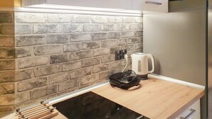 Eine Küche mit Ziegelrückwand, einem Edelstahl-Kühlschrank, einem Wasserkocher und einer schwarzen Induktionskochplatte.