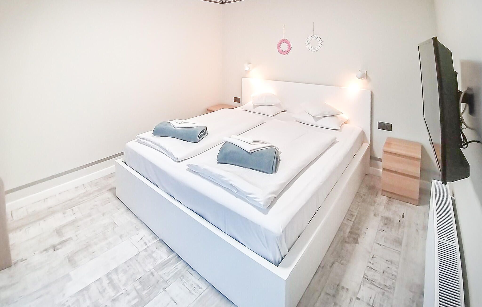 A modern bedroom with a large bed, white bedding, and a flat-screen TV mounted on the wall.