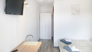 Hotellihuone, jossa on sänky, työpöytä, tuoli, televisio ja ovi, joka johtaa toiseen huoneeseen.