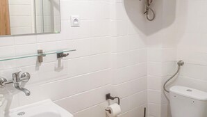 Un bagno con pareti piastrellate di bianco, uno scaffale in vetro, un lavandino, un water e uno specchio.