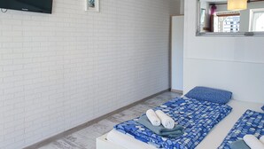 Una camera da letto con parete in mattoni bianchi, un letto con lenzuola blu, una TV, un quadro incorniciato e uno specchio.