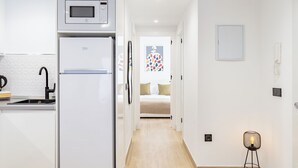 Una cucina moderna con forno a microonde e frigorifero integrati, un lavello con rubinetto nero e un corridoio che conduce a una camera da letto con un letto e un'allegra decorazione a parete.