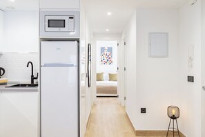 A modern kitchen with a built-in microwave and refrigerator, a sink with a black faucet, and a hallway leading to a bedroom with a bed and a colorful wall decoration. - Sun Duplex Fuengirola (Fuengirola)