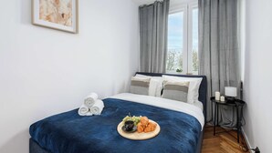 Un lit bien fait, recouvert d’une couverture bleue, une table de chevet avec une lampe, et une assiette de nourriture posée sur le lit.