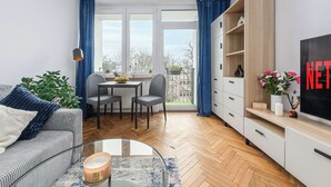 Un salon moderne comprenant un canapé, une table basse en verre, un coin repas avec une table et des chaises, un téléviseur et une grande fenêtre avec des rideaux.