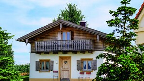 A two-story chalet with a balcony, wooden shutters, and a small garden. - Ferienhaus im Landhausstil im Vital Camp Bayerbach (Bayerbach)