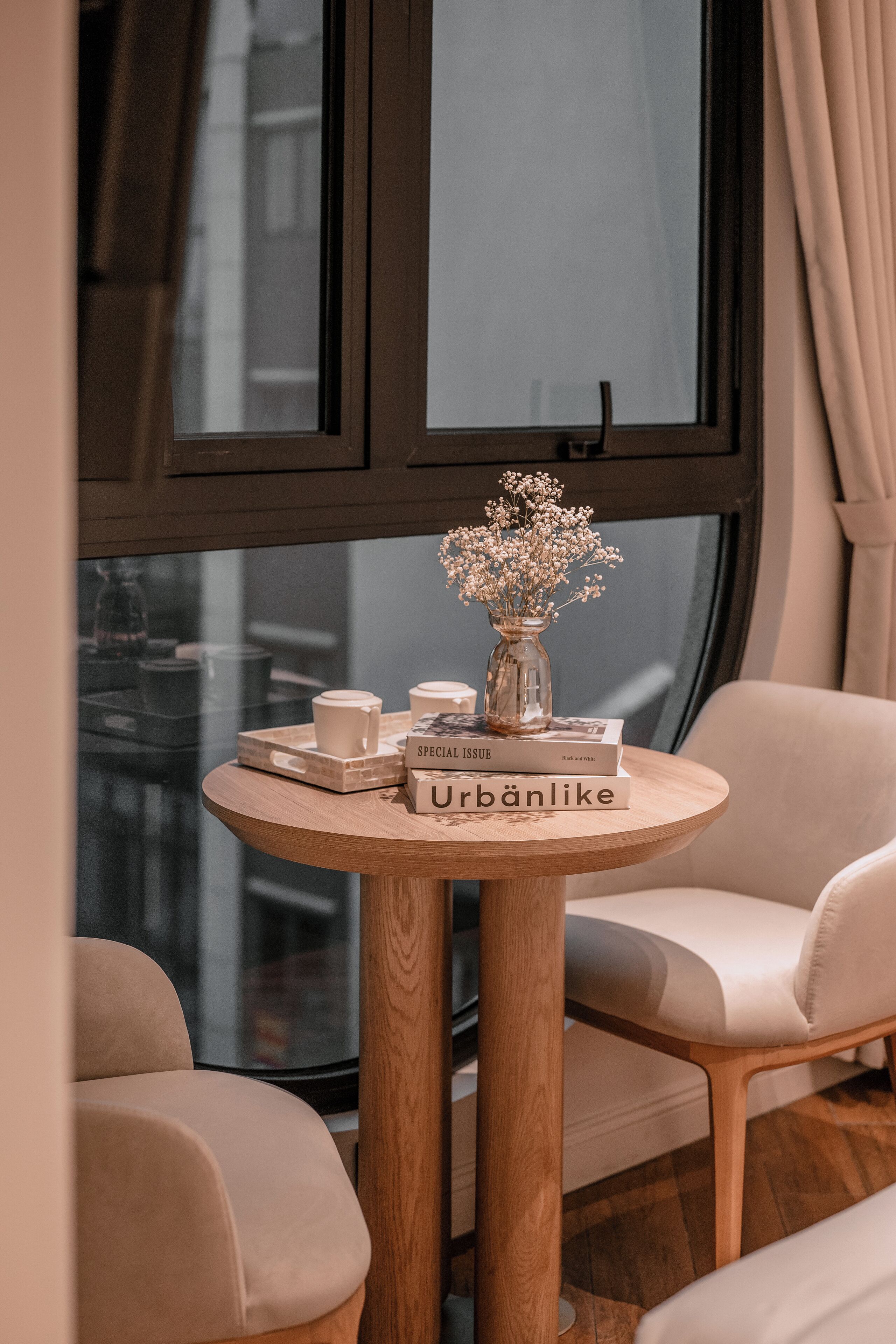A round wooden table with a vase of flowers, a mug, and books.