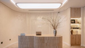 A reception desk with a laptop, a vase with branches, and a wooden cabinet with decorative items. -  iRest Atelier Hanoi Apartment & Hotel (Hanoi)