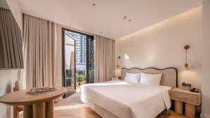 A modern hotel room with a large bed, a wooden side table, a small desk, and a view of the city through the window. -  iRest Atelier Hanoi Apartment & Hotel (Hanoi)