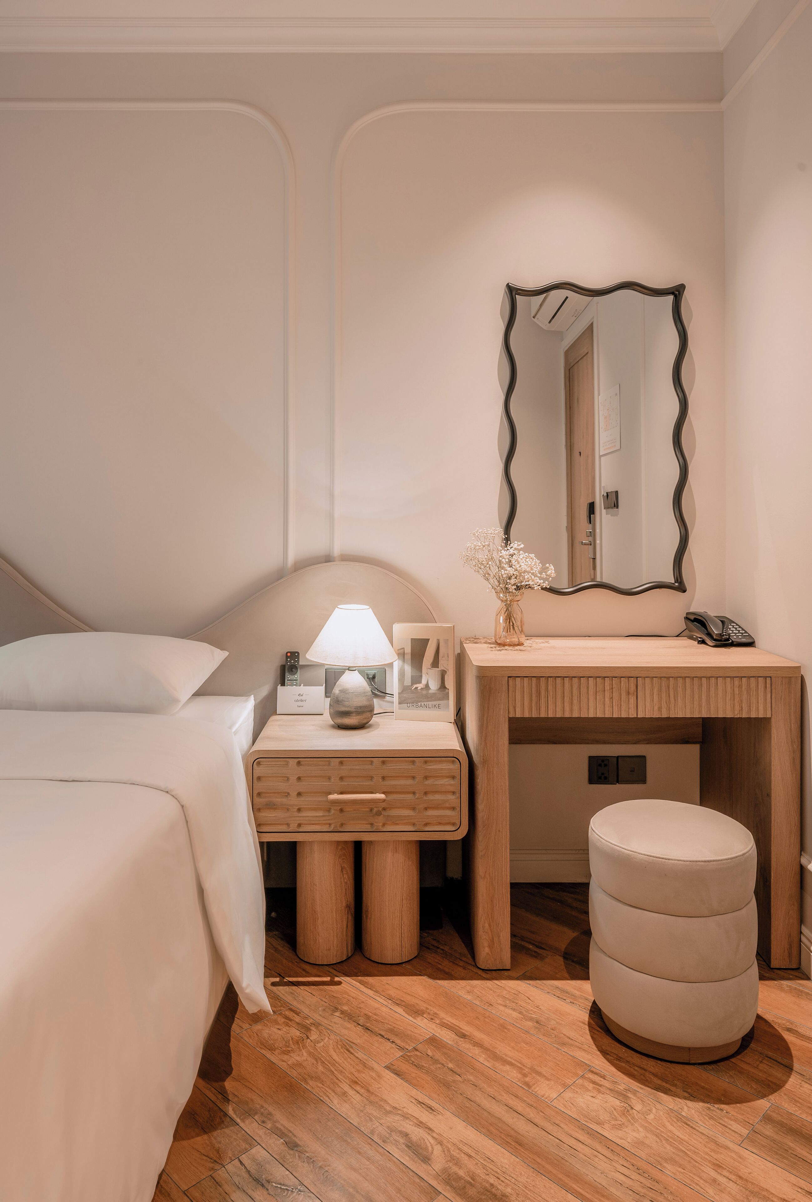 A bedroom with a bed, a wooden dresser, a vanity with a mirror, and a small stool.