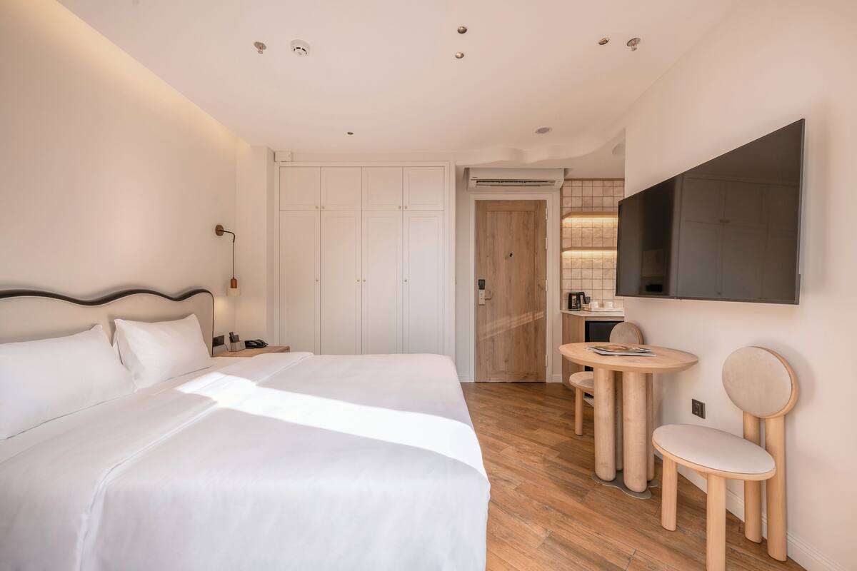 A hotel room with a large bed, a small table, a chair, and a TV mounted on the wall.