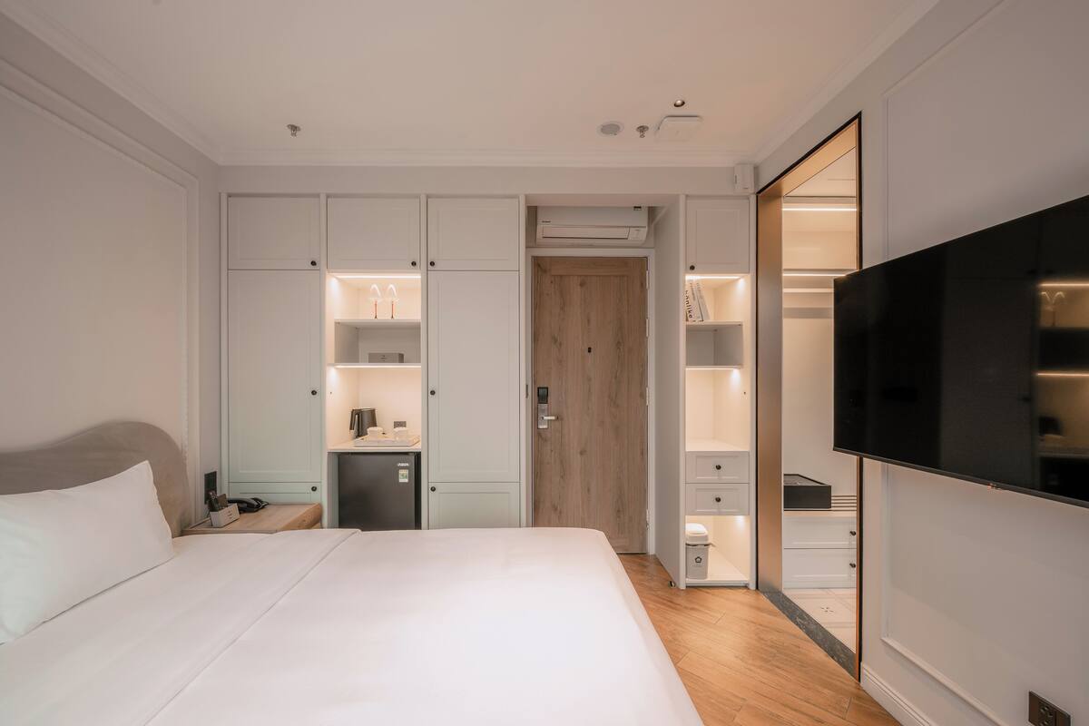 A modern hotel room with a large bed, built-in wardrobe, and a flat-screen TV.
