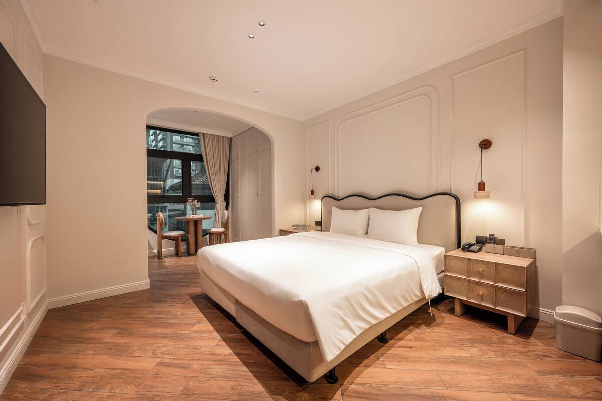 A hotel room with a large bed, bedside tables, a TV, and a view of the outside.