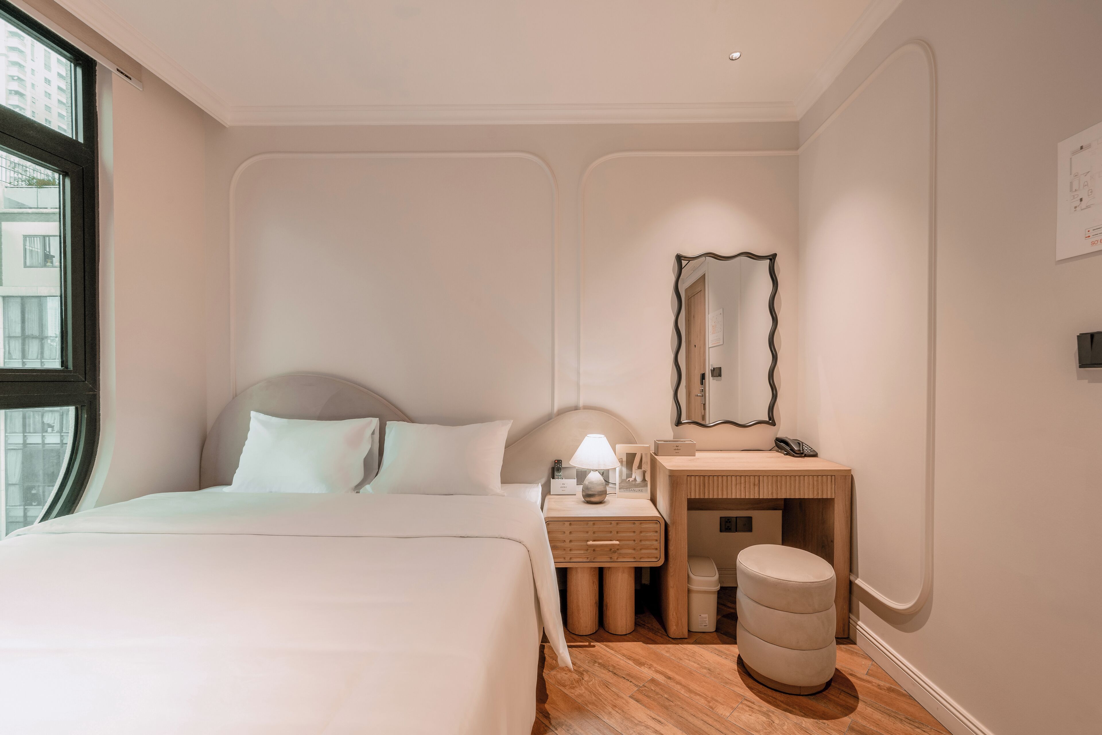 A modern bedroom with a bed, bedside table, mirror, and a small stool.