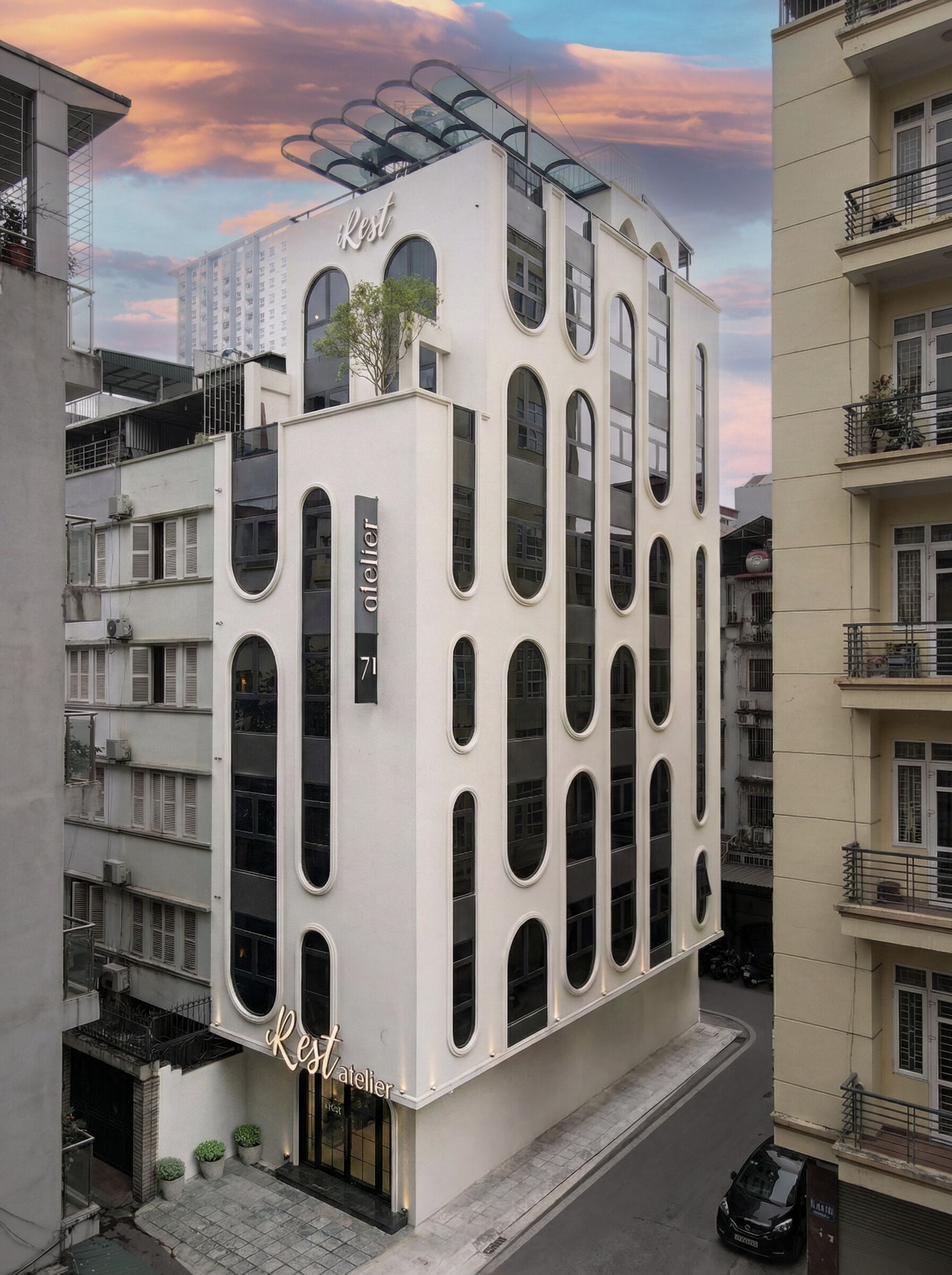 Un bâtiment moderne à la façade blanche, doté de nombreux balcons et d’un jardin sur le toit.