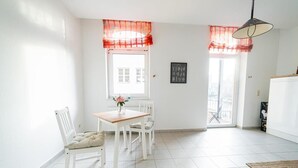Et lyst spiseområde med et hvidt bord og stole, en vase med blomster og et vindue med rød gardin.