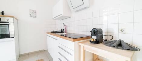 A modern kitchen with white cabinetry, a black countertop, and a coffee machine.