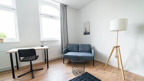 En moderne stue med et skrivebord, en grå sofa, en gulvlampe og et vindue med gardiner.