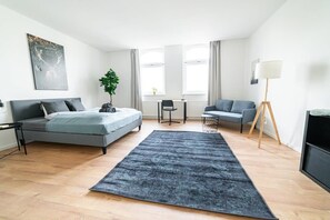 Un dormitorio moderno con cama, escritorio, silla, sofá y lámpara de pie.