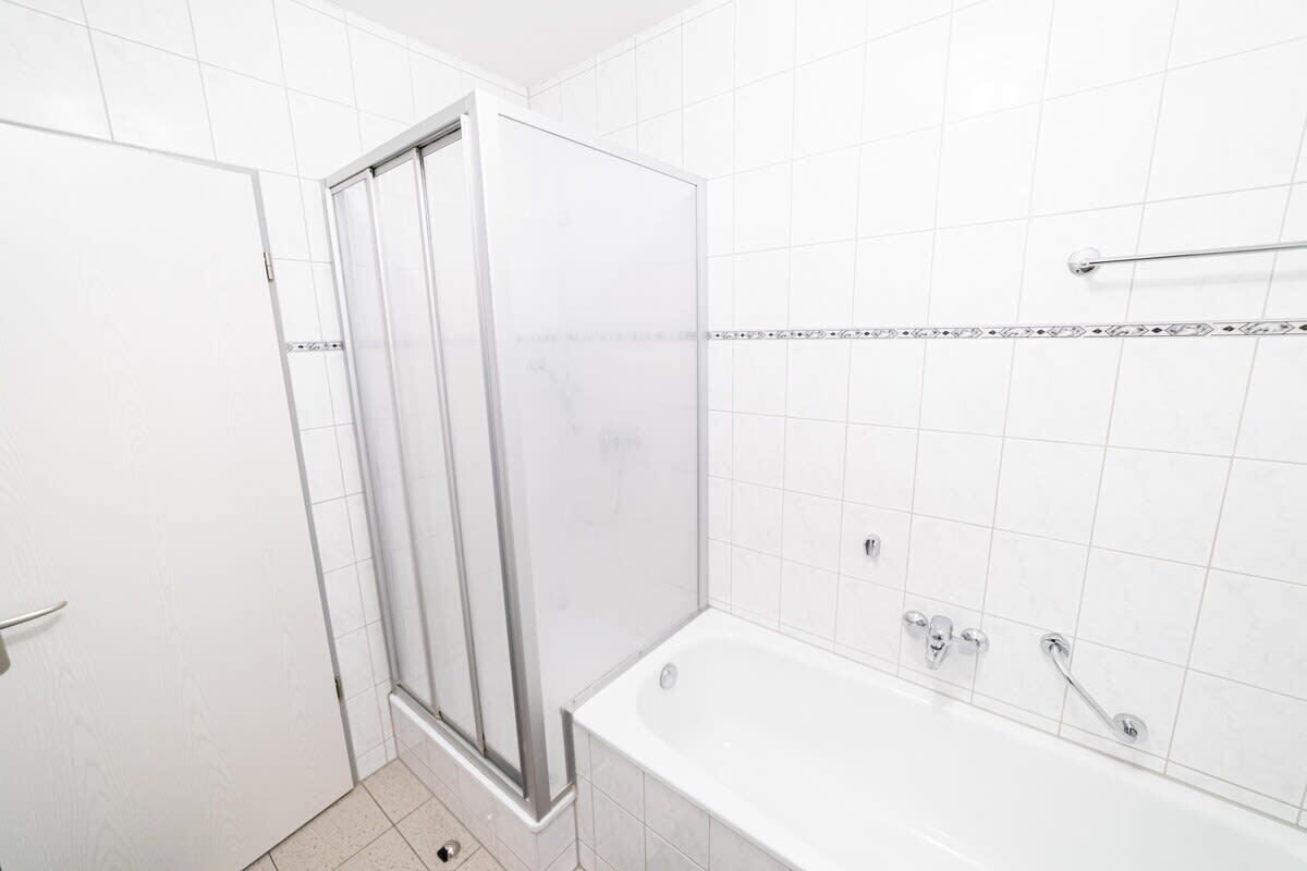 Une salle de bain avec une douche à parois de verre, une baignoire et des murs recouverts de carreaux blancs.