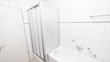 Une salle de bain avec une douche à parois de verre, une baignoire et des murs recouverts de carreaux blancs.