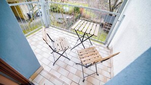 Un balcón con dos sillas de madera y una mesa, con vista a un jardín y un edificio.