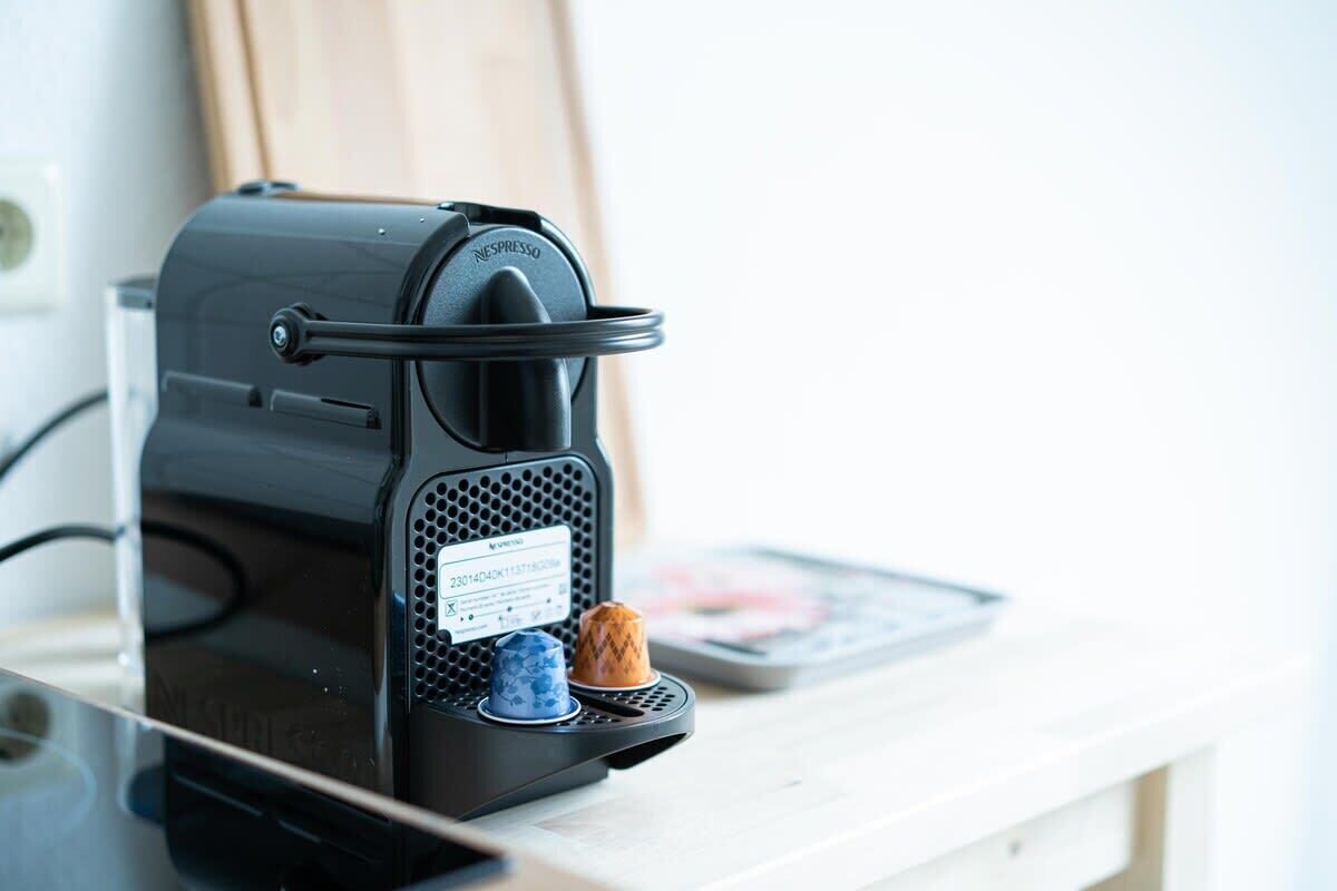 Eine schwarze Nespresso-Kaffeemaschine auf einer weißen Arbeitsplatte mit einem kleinen, blau-braunen Kaffee-Pad-Halter.