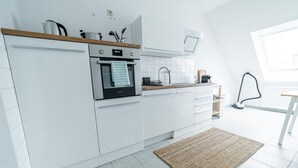 A modern kitchen with white cabinets, a built-in oven, and a window above the sink. - FullHouse | Magdeburg | L10-5 | RoofTop (Magdeburg)