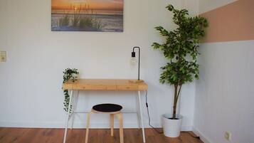A room with a wooden desk, a black chair, a potted plant, and a wall-mounted lamp.