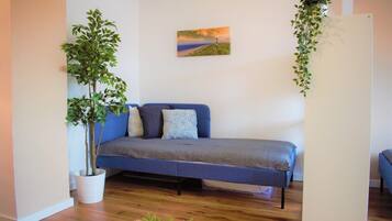 A modern bedroom with a blue sofa bed, a large potted plant, and a painting on the wall.