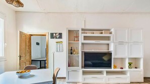 Ein modernes Wohnzimmer mit Essbereich, weißen Schränken, einem Flachbildfernseher und Holzboden.